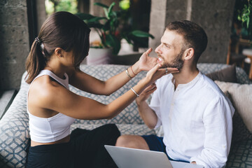 Woman playfully touching male freelancer’s beard while he uses laptop, showing friendly connection, trust and relaxed tech-based partnership in creative freelance environment with digital tools.