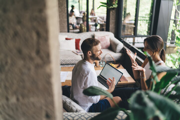 Two freelancers gesturing during digital planning session, using laptops to brainstorm ideas,...