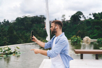 Freelancer gesturing during video call with wireless earbuds, confidently communicating ideas in...