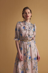 Fashionable woman in a soft pink maxi dress with blue floral patterns and elegant ruffles, posing...