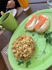 Outdoor breakfast: scrambled eggs with vegetables and bacon, salmon sandwiches with cream cheese on baguette slices, green tea and orange juice.