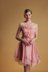 Graceful woman poses in a short strapless pink organza dress with a flower accent at the waist,...