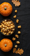 Caramel popcorn, pumpkins, oak leaves on black background, autumn