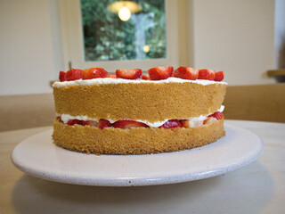 Layered strawberry cake with whipped cream and cut strawberries, shown from front view with fruit and cream details.