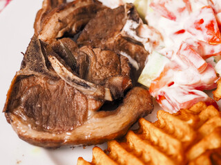 Dinner meal with cooked lamb loin chops, potato lattice and fresh salad with sour cream. Close up....