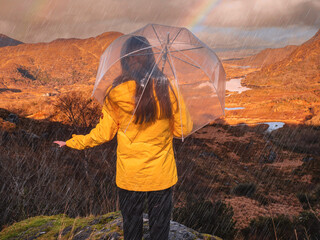 Teenager girl in yellow jacket and umbrella and enjoys stunning mountain view in Killarney area of...