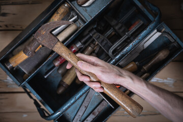 Top-down view of old beige wooden table with chipped paint showing hand holding vintage hammer with...