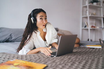 Woman reacts with surprise during video call while using laptop and headphones, portraying...