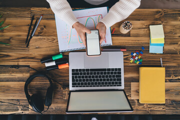Millennial freelancer typing on smartphone while multitasking with laptop, showing modern...
