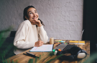 Confident freelancer smiling while developing visual project on graph paper with laptop, embodying...