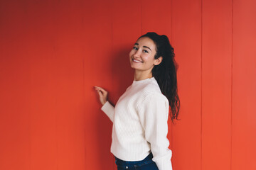 Cheerful young Middle Eastern woman standing by red wall, smiling with confidence, representing...