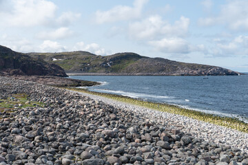 Rocky Arctic coastline with layered moss-covered stones, crashing waves, and rugged green hills in...