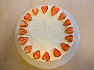 Overhead view of a strawberry cake topped with whipped cream and halved strawberries arranged in a decorative circle.