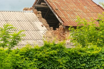 fragment of a destroyed brick wall of an old barn under a slate roof on a sunny summer day