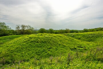 the remains of an ancient citadel in the form of a hill and a concentric ditch, covered with green grass, from the late Bronze Age in a field in southern Russia on a sunny day