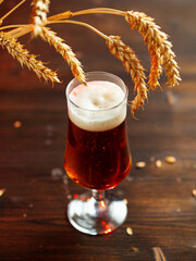 Light beer glass on wooden table, ears of wheat