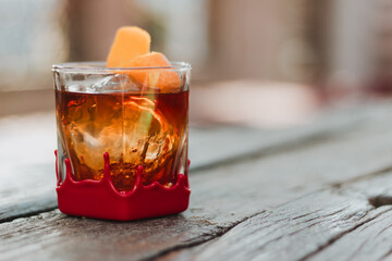Hand-dipped red-wax-base rock glass with amber cocktail, ice sphere, and orange-peel garnish on rustic wooden surface