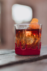 Vertical close-up of red-wax-dipped rock glass with amber cocktail, ice sphere, and orange-peel twist on weathered wooden tabletop