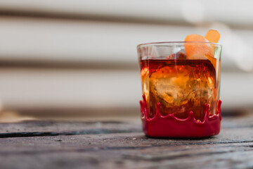 Red-wax-dipped rock glass with amber cocktail, spherical ice, and orange-twist garnish on weathered wooden table with blurred background