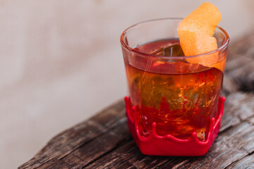 Angled close-up of red-wax-dipped rock glass with amber cocktail, spherical ice, and curled orange-peel garnish on weathered wooden table