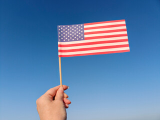 Hand Holding Small American Flag on Blue Sky Background. Concept of patriotism, personal freedom,...