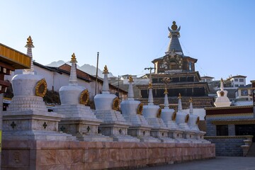 Eight white stupas aligned at Taktsang Lhamo Monastery (Langmusi), a sacred Tibetan Buddhist site in the Amdo region, renowned for its spiritual and architectural heritage.