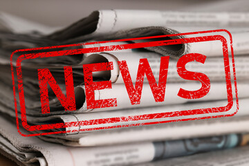 Red News stamp and many newspapers on table, closeup