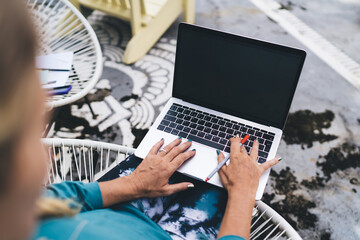 Over-the-shoulder view of woman typing on laptop with pen, showcasing remote tech use and focused...