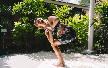 Blonde woman smiling in revolved chair pose, hands in prayer at heart center, twisting with...