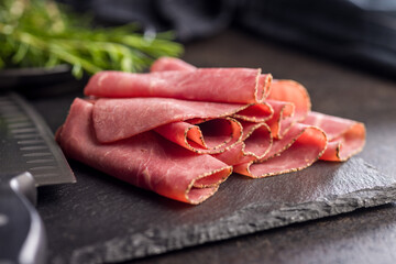 Sliced beef pastrami on cutting board on black table.