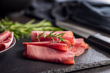 Sliced beef pastrami on cutting board on black table.