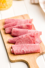 Sliced beef pastrami on cutting board on white table.