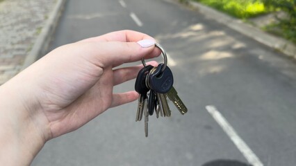 A bundle of keys held by a woman's hand, close-up, against the background of the road