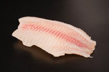 Fresh tilapia fillet on black background, top view.
