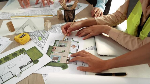 Smart architect and safety engineer discussion about building blueprint on table with architectural document, measurement tools and wooden block scatter around at modern office. Closeup. Delineation.