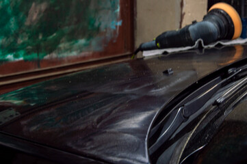 A person is polishing a dark car surface, using a power buffer, to achieve a glossy finish in a...