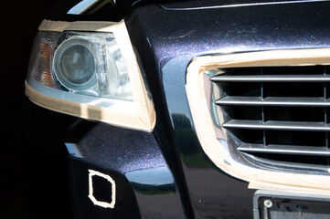 Careful polishing of a car's front end with focus on headlight and grille area, showcasing masking...