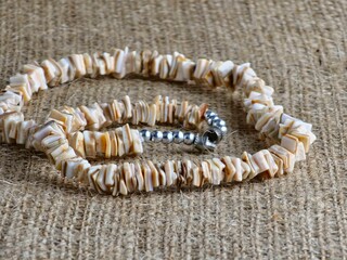 Handmade polished beige shell pieces necklace as gift for a woman on a beige background. Natural jewelry. Summer jewelry.
