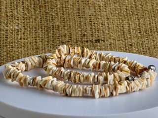 Handmade polished beige shell pieces necklace as a gift for woman on beige background. Natural jewelry. Summer jewelry.