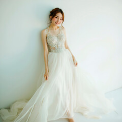 Fototapeta premium Young female model standing in luxurious long designer dress with chiffon haute couture against plain white wall. Professional portrait shooting for fashion magazine