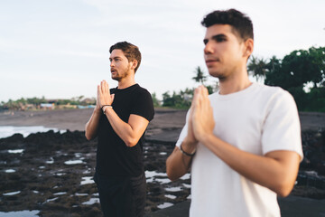 Focused male yoga partners practice still posture at shoreline, embodying dual awareness, shared...