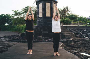 Yoga duo reaches upward with palms pressed, standing tall at sacred site, illustrating aligned...