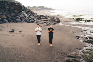 Two men stand barefoot in prayer pose on open beach, symbolizing inner stillness, masculine...