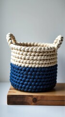 A woven basket with blue and natural fibers sits on a wooden block against a white background. backdrop