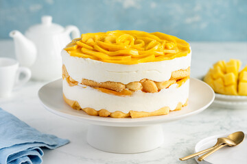 Round whole tiramisu cake with mango on a stand on a marble table. Famous Italian dessert with...