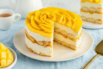 Round tiramisu cake with mango on a plate on a blue tablecloth. Variation of the Italian dessert...