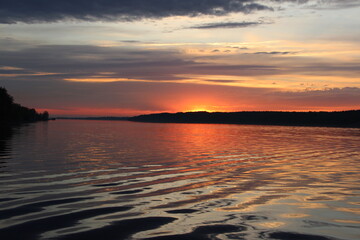 Tranquil Sunset Over Calm Water with Vibrant Orange and Purple Sky Reflections and Dock Extending Toward Tree-Lined Horizon