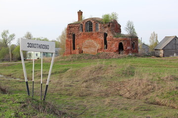 Ruined Brick Building with Chimney and Arched Windows in Overgrown Field, Sign and Trees under...
