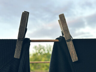 Clothespins secure dark garments on a drying rack against a cloudy sky, featuring a serene outdoor...