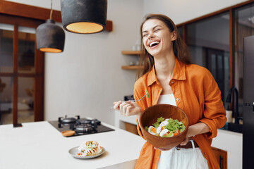 Joyful young woman enjoying a healthy salad in a modern kitchen, showcasing vibrant colors and a...